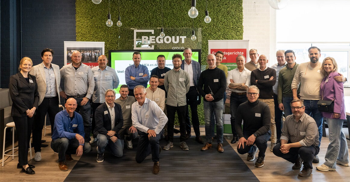 Groepsfoto deelnemers kennissessie MEA bij Thomas Regout - deelnemers staan in halve cirkel naast elkaar en een aantal mensen zitten gehurkt op de foto staan 27 personen